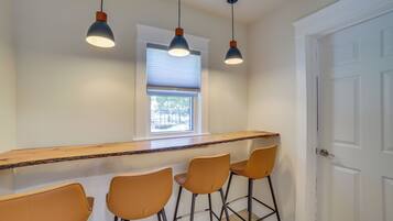 A kitchen with a bar area, three bar stools, a window with blinds, and a door.