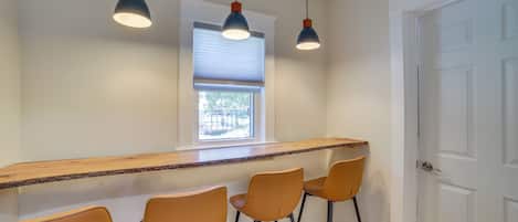 Una cocina con barra, tres taburetes de bar, una ventana con persianas y una puerta.