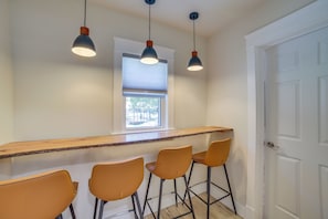 A kitchen with a bar area, three bar stools, a window with blinds, and a door.
