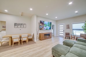A modern living room with a wooden dining table, chairs, a flat-screen TV, a fireplace, and a green sofa.