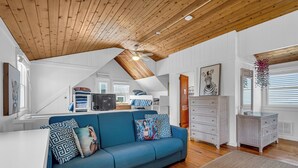Uma sala de estar ampla, com um sofá azul, teto de madeira e paredes brancas.