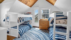 Quarto com teto inclinado, beliches, cômoda e janela.