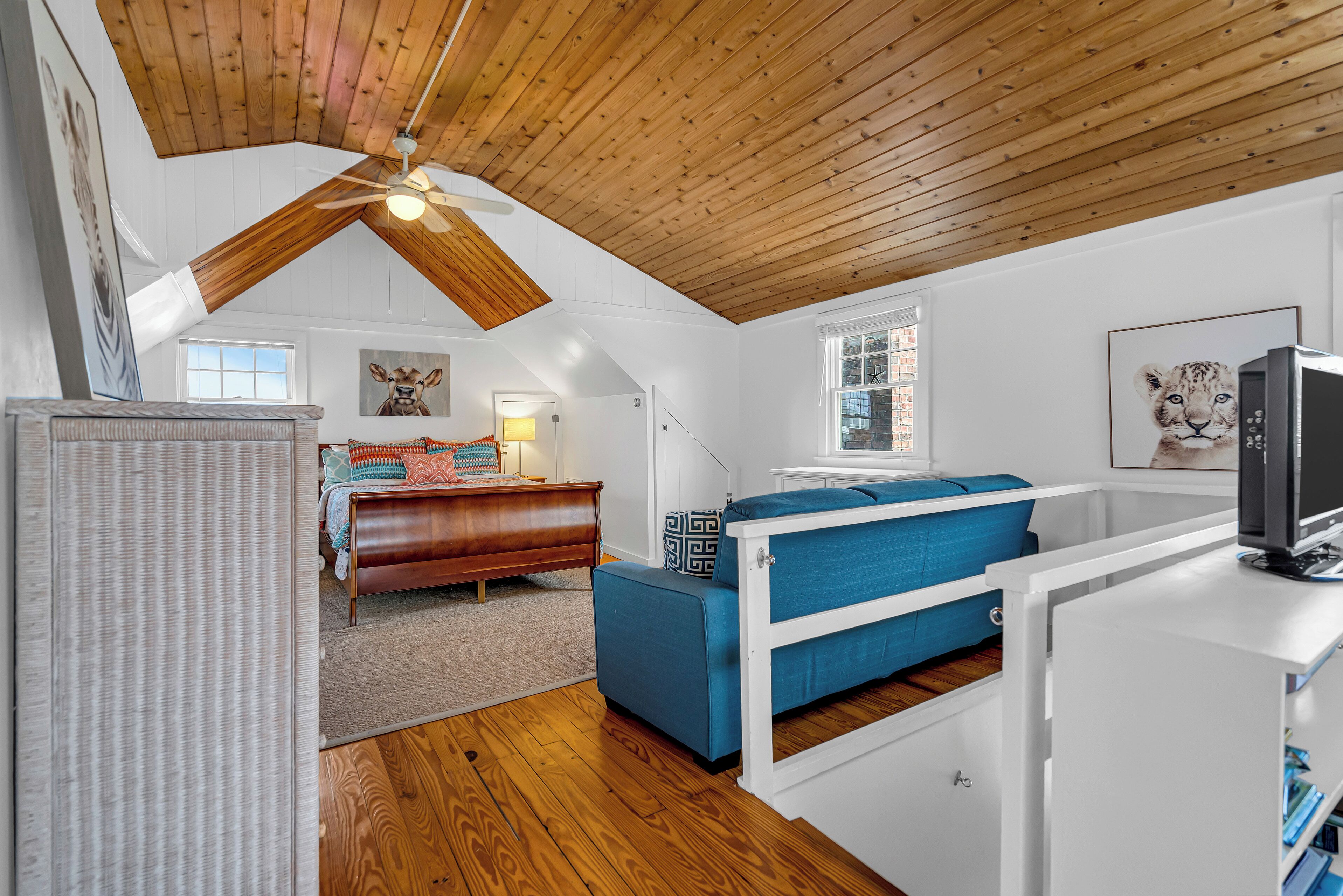 A bedroom with a sloped ceiling, a bed, a desk, and a television.