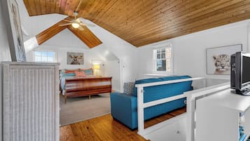 A bedroom with a sloped ceiling, a bed, a desk, and a television.