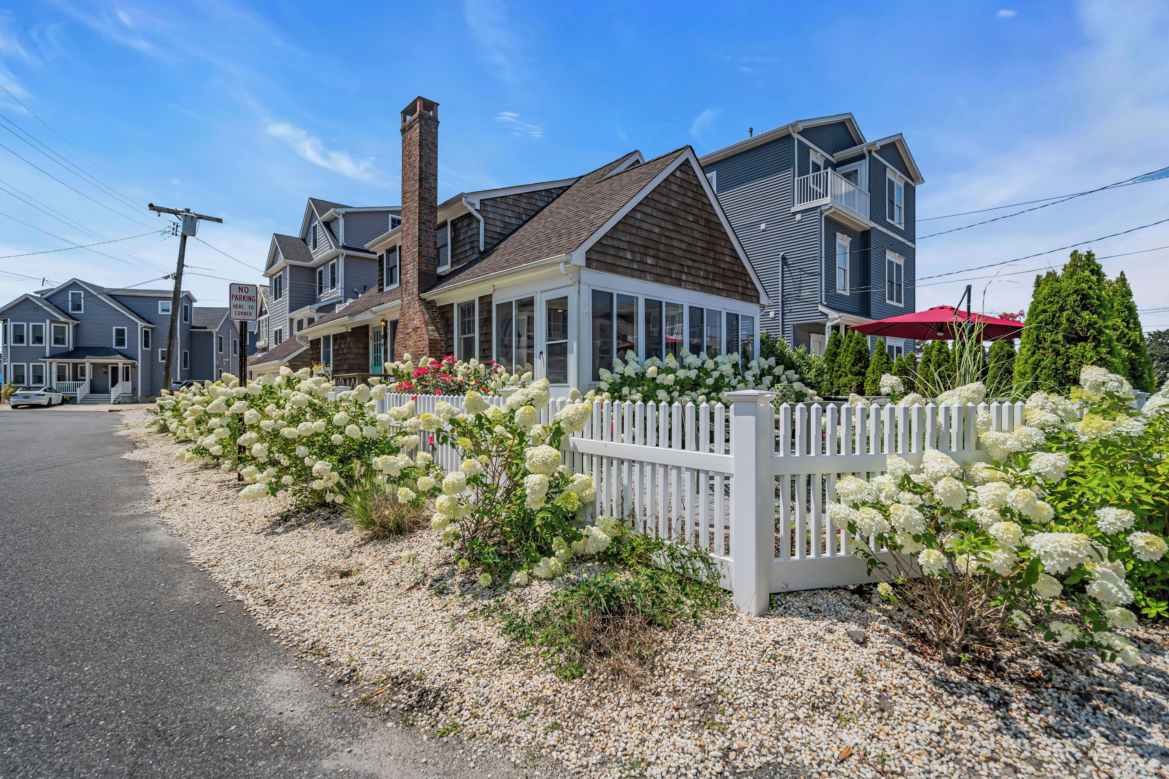 A residential area with houses, a gravel driveway, and a white picket fence.