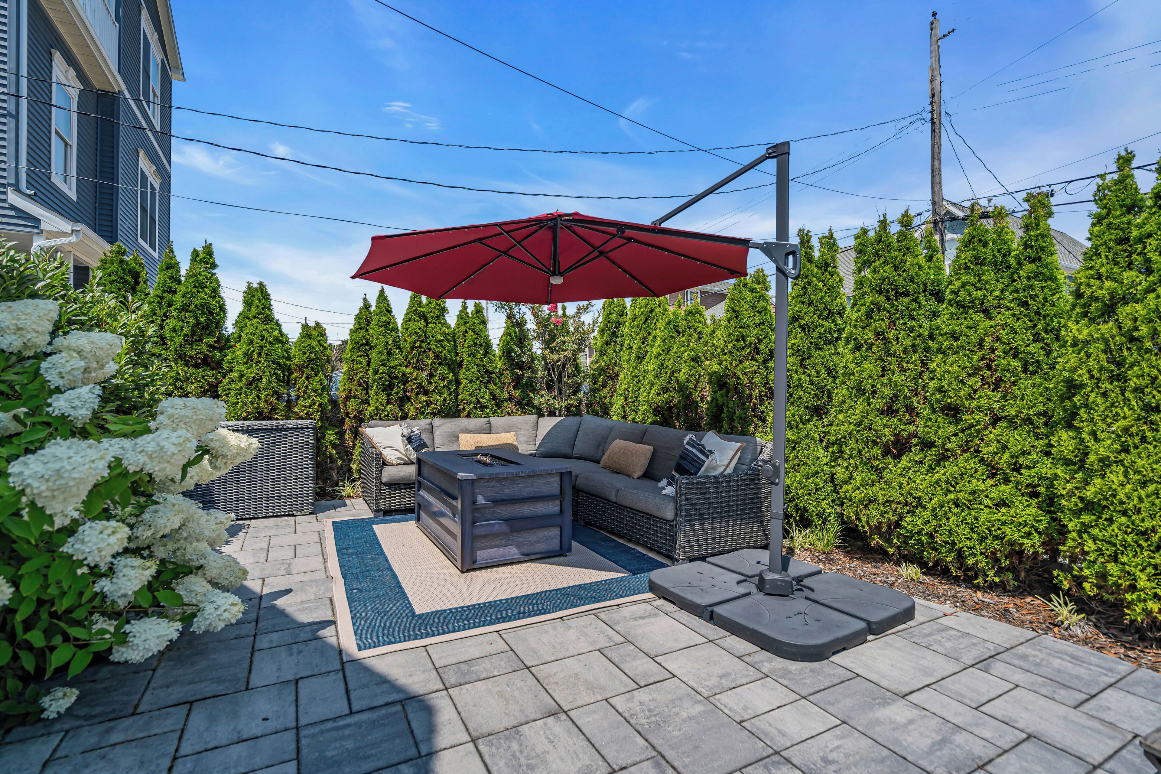 A patio with a gray sofa, a red umbrella, and a stone-tiled floor.