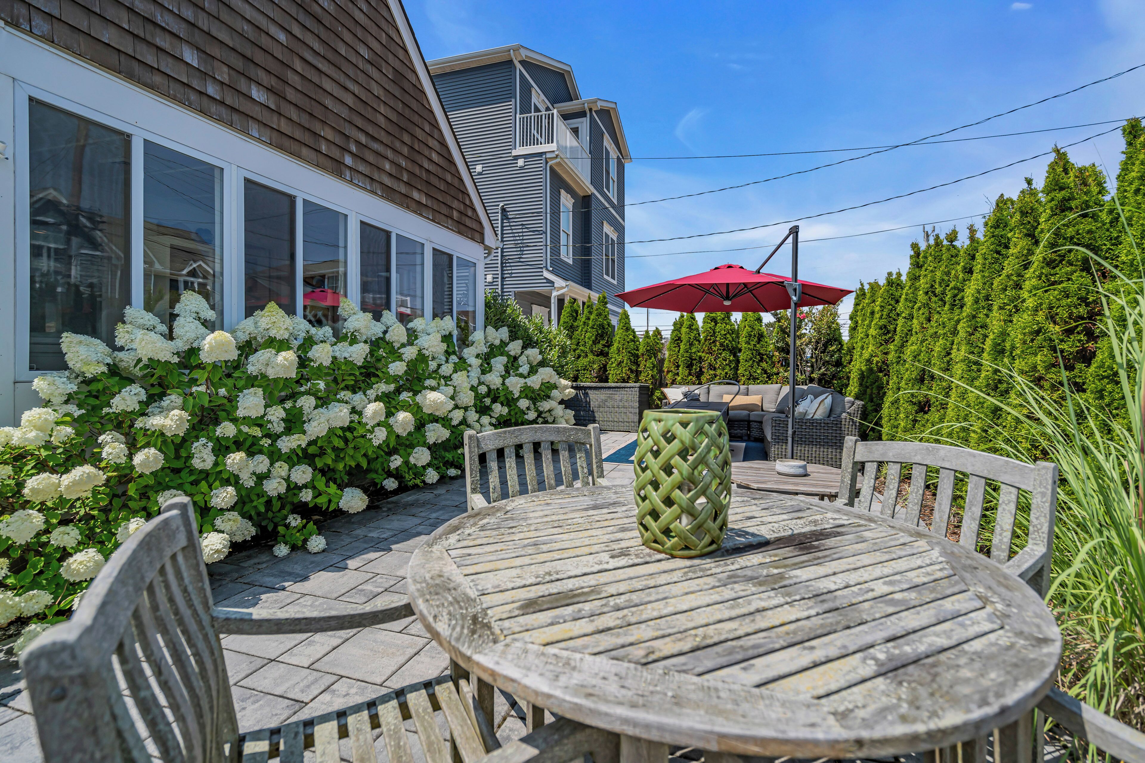 Un patio con una mesa y sillas de madera redonda, rodeado de arbustos de hortensias blancas.