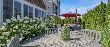 Un patio con una mesa y sillas de madera redonda, rodeado de arbustos de hortensias blancas.