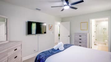 A bedroom with a bed, a television, a ceiling fan, a dresser, and a bathroom visible through an open door.