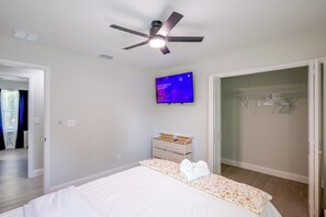 Un dormitorio con cama, ventilador de techo, televisor montado en la pared y vestidor con ropa colgada.
