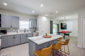 A modern kitchen with grey cabinets, a central island, and a dining area with a pool table.