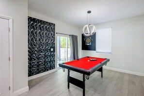 Una mesa de billar con un dardo en una habitación con pared de diseño geométrico y ventana con persianas.