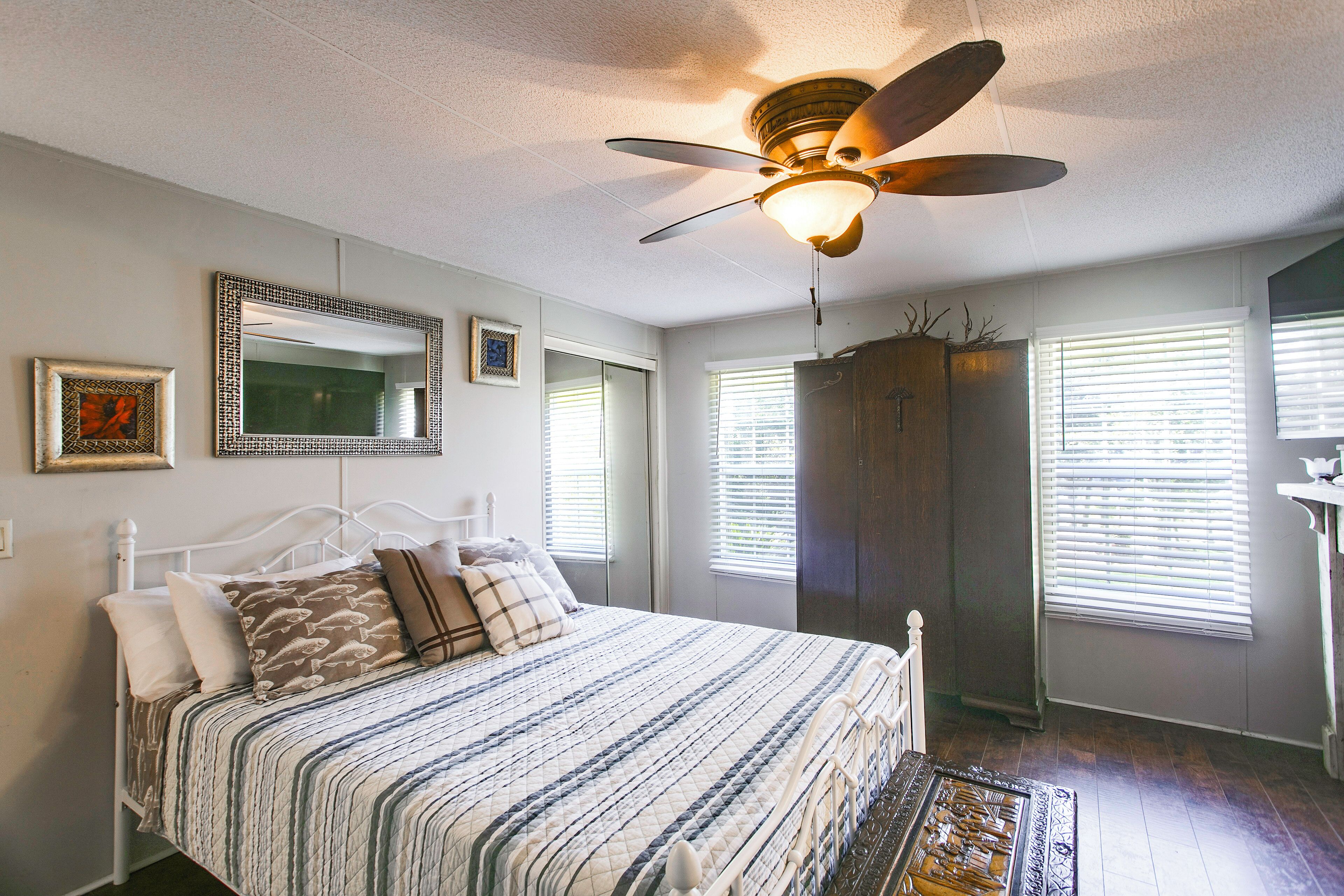 A bedroom with a bed, a ceiling fan, a wardrobe, and a window with blinds.