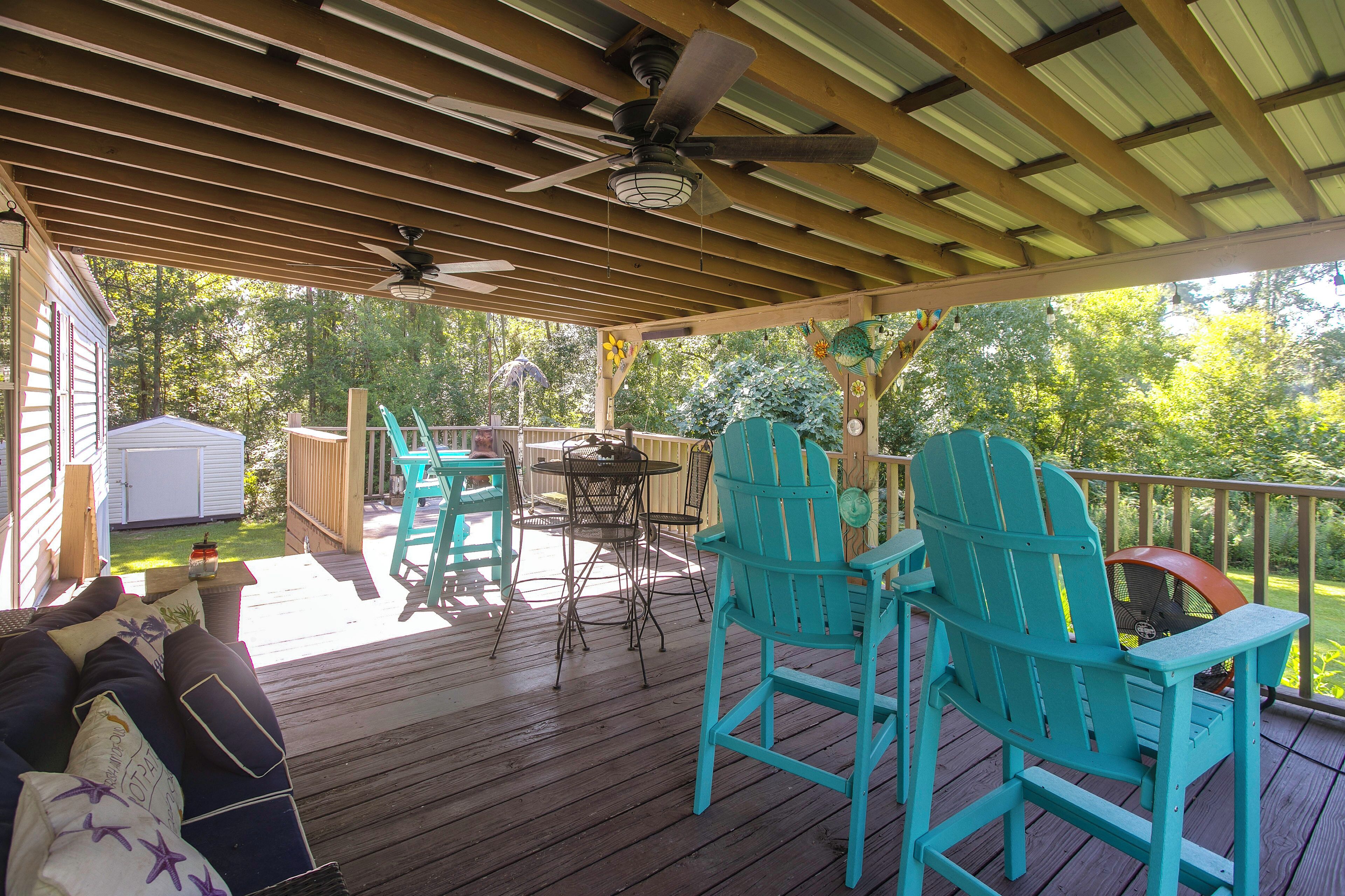 A covered outdoor deck with wooden flooring, a ceiling fan, and turquoise Adirondack chairs.