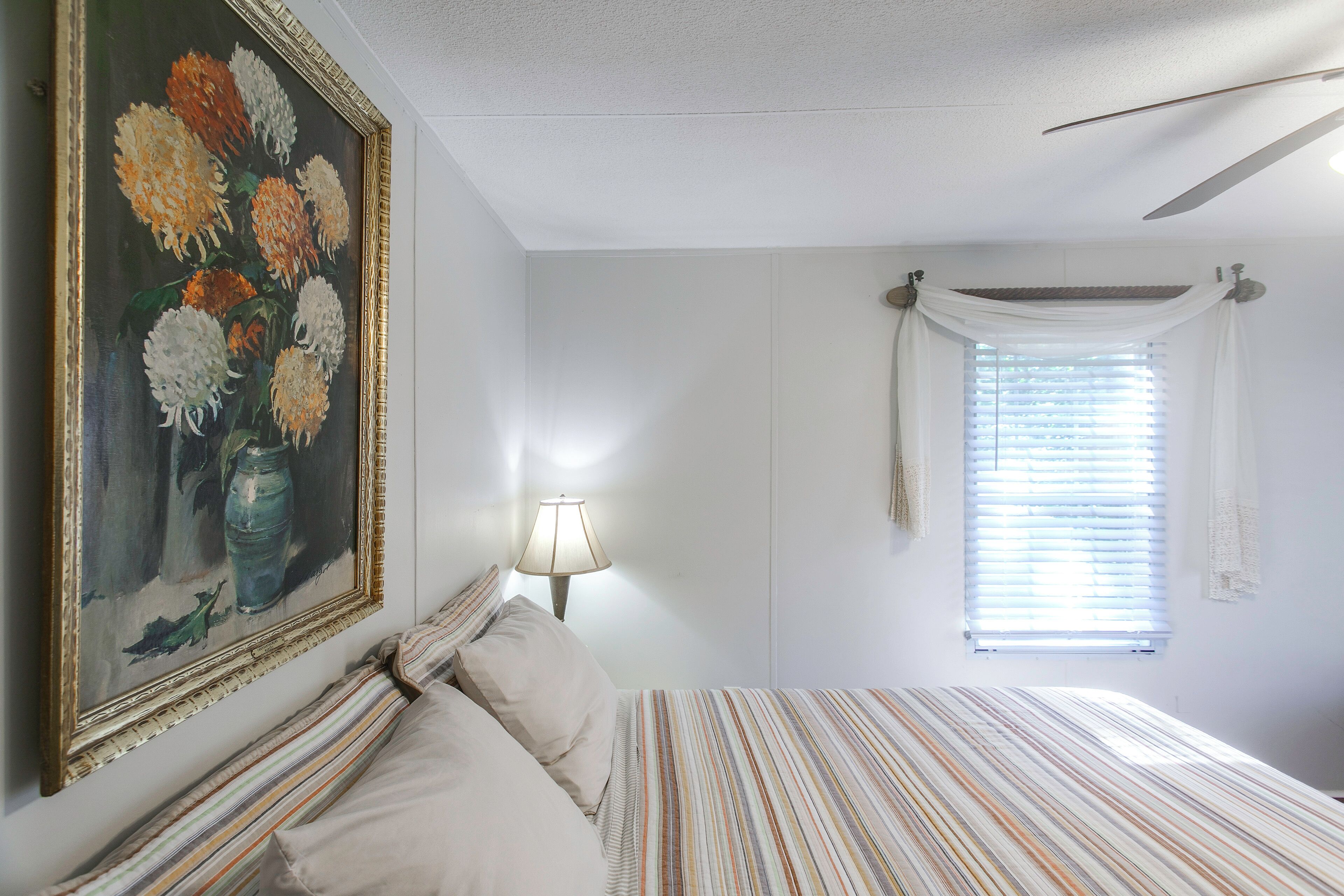 A bedroom with a bed, a painting, a lamp, and a window with curtains.