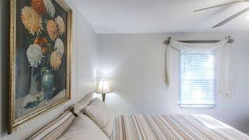 A bedroom with a bed, a painting, a lamp, and a window with curtains.