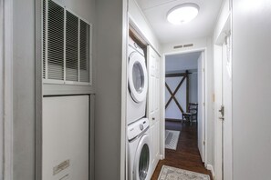 Un lavadero con lavadoras y secadoras apiladas, una rejilla en la pared y piso de madera.