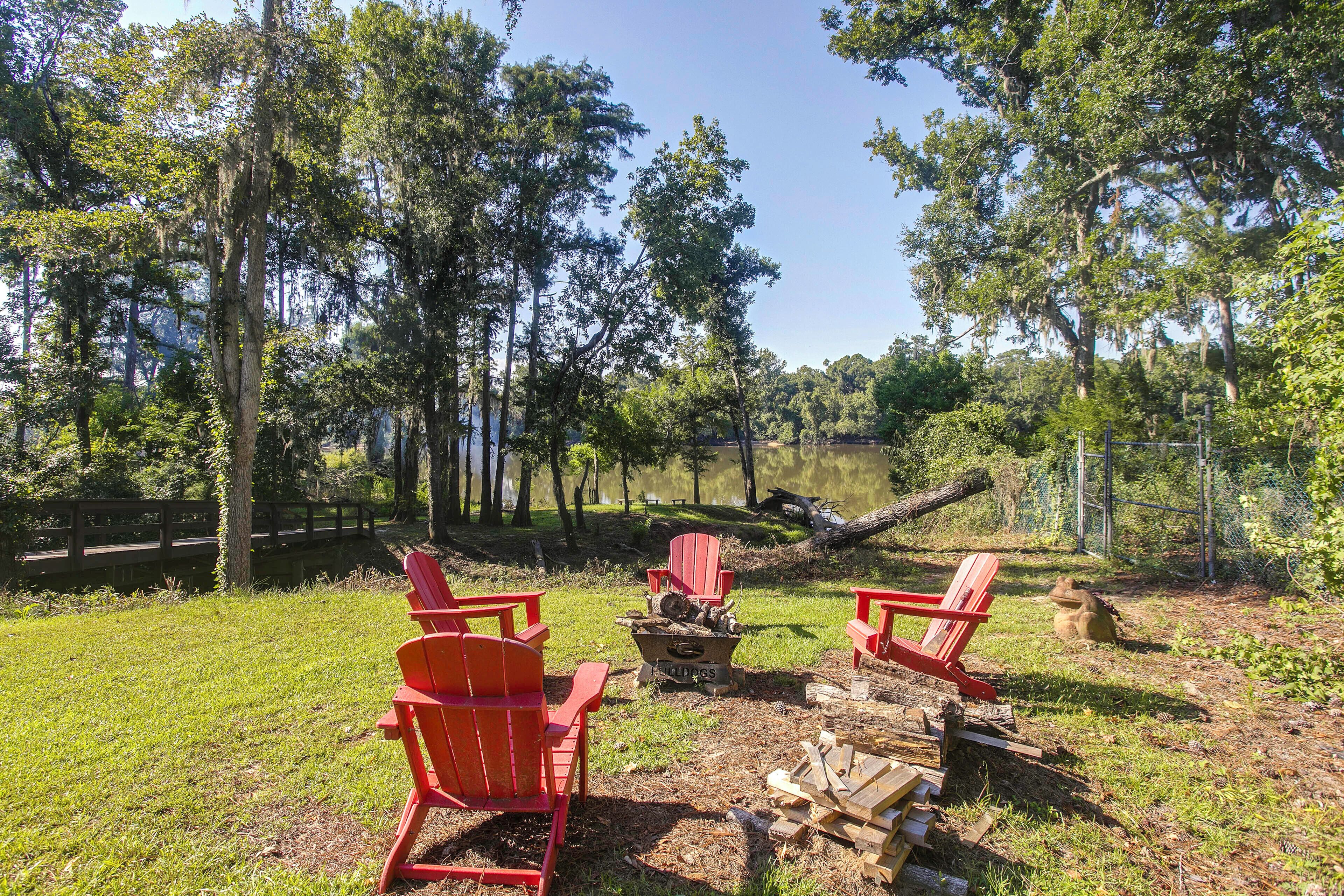 A campsite with red Adirondack chairs arranged around a fire pit.