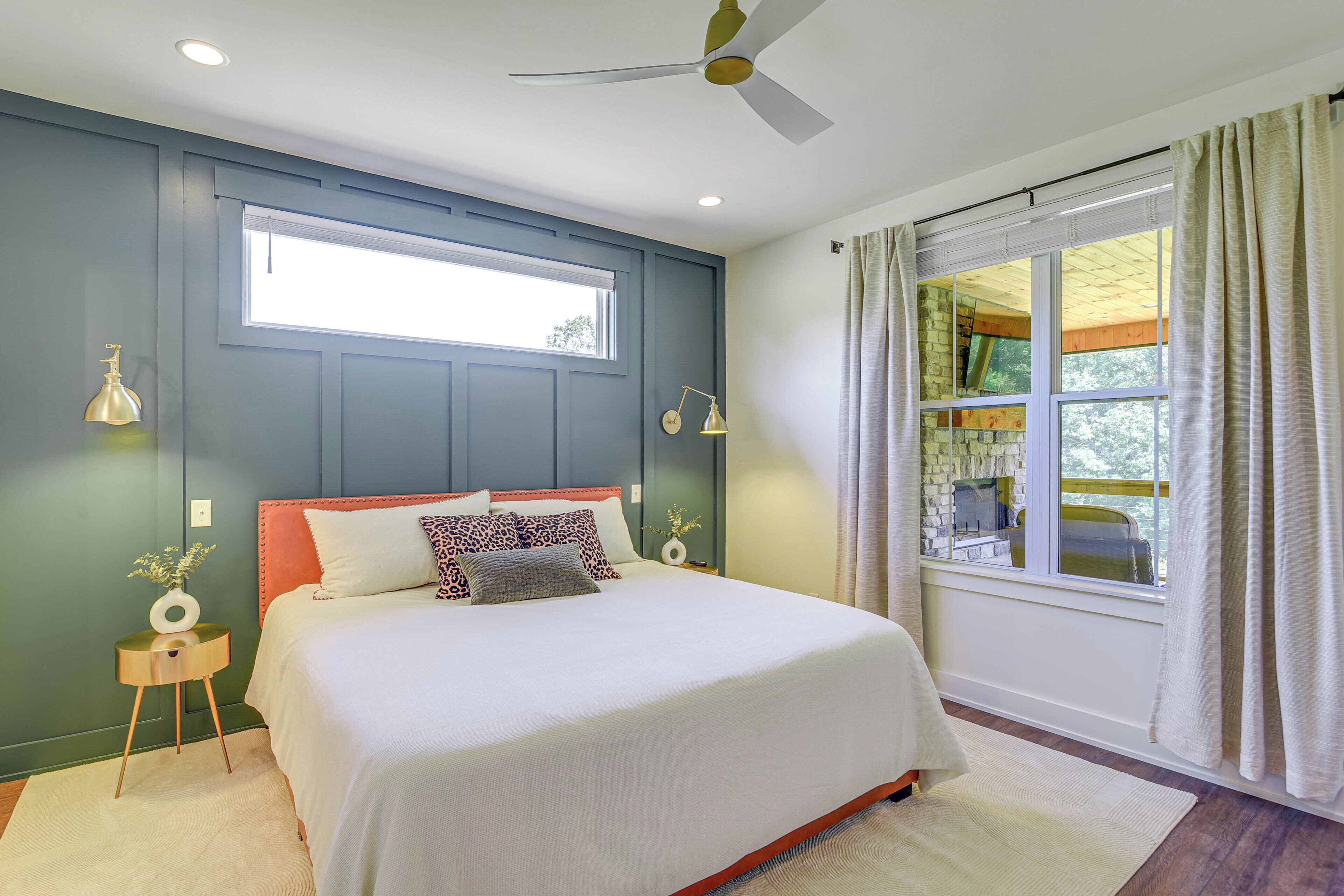 A bedroom with a bed, a ceiling fan, a window with curtains, and a view of the outdoors.