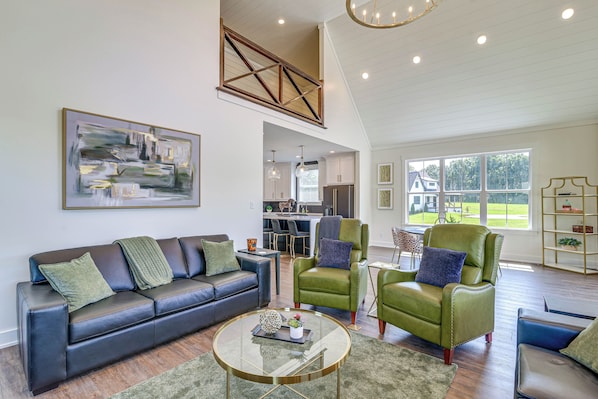 A spacious living room with a high ceiling, a dining area, and a kitchen visible through an open door. - Brand New, Hot Tub & Porch, Near Nolin Lake! (Clarkson)