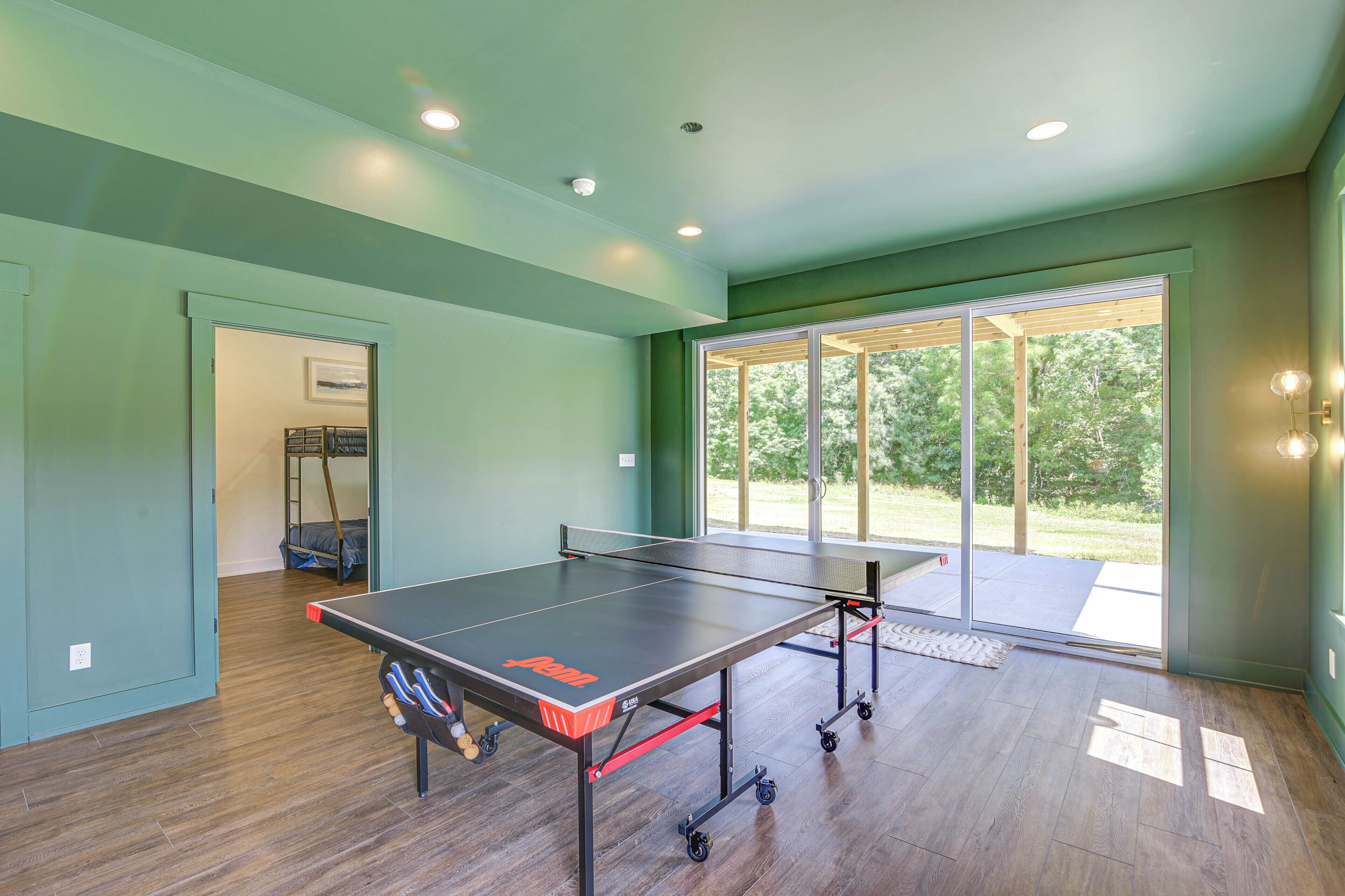 A ping pong table with wheels in a room with wooden flooring and a view of a garden through a glass door.