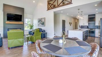 A modern kitchen with a central island, a dining area with a round table, and a living room with green sofas.