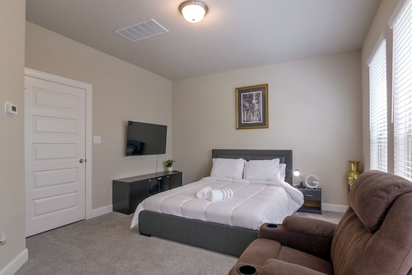A bedroom with a bed, a bedside table, a lamp, a chair, and a window with blinds. - Modern Efficiency Studio Near NRG & Medical Center (Houston)