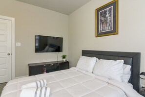 A hotel room with a bed, a television mounted on the wall, a framed picture above the bed, and a door on the left. - Modern Efficiency Studio Near NRG & Medical Center (Houston)