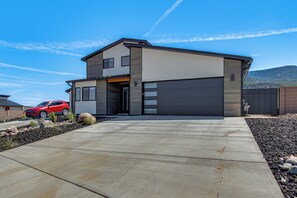 A modern two-story house with a garage, a driveway, and a red car parked in the driveway. - Game Room & Stunning Mtn Views! Cedar City Home (Cedar City)