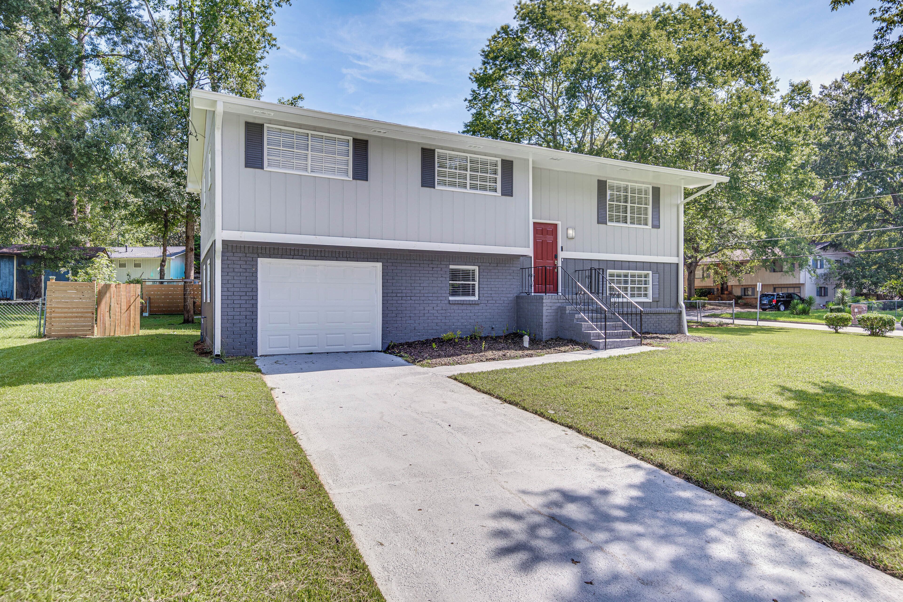 A two-story residential building with a garage, a red door, and a front yard.