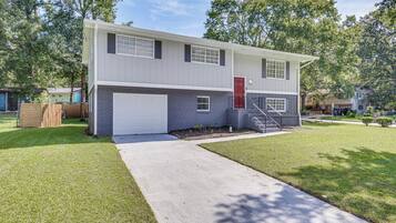 A two-story residential building with a garage, a red door, and a front yard.