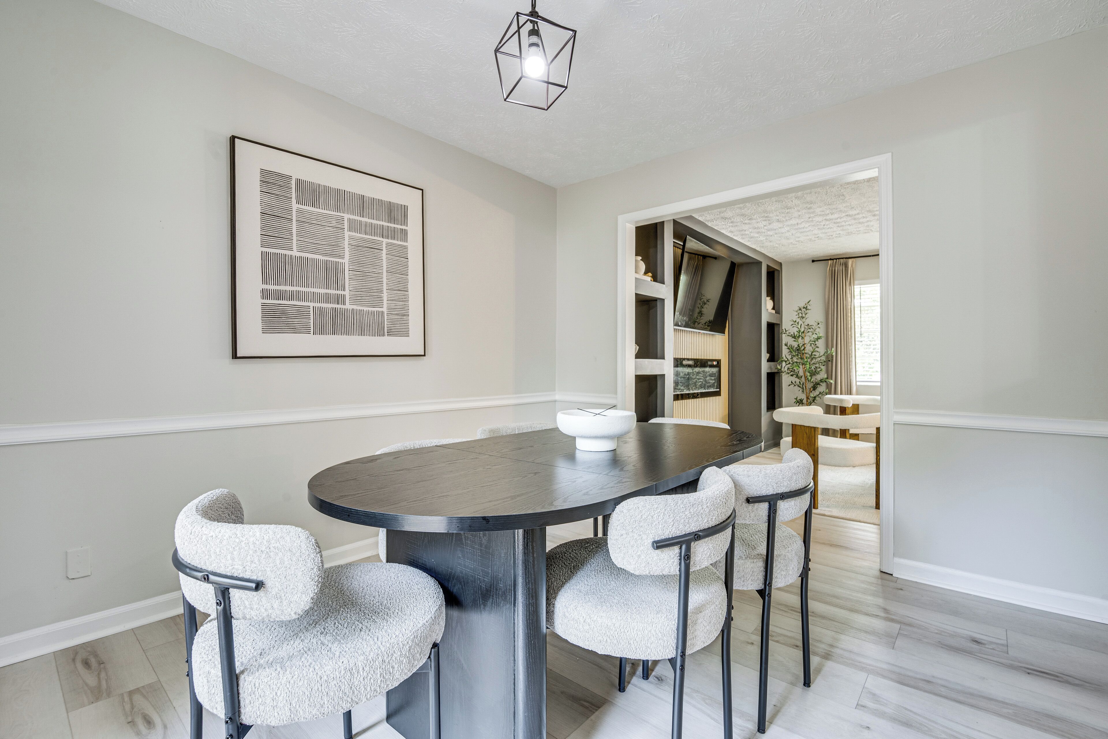 A dining area with a round table, four chairs, a wall-mounted light fixture, and a framed abstract artwork.