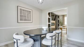 A dining area with a round table, four chairs, a wall-mounted light fixture, and a framed abstract artwork.
