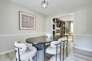 A dining area with a round table, four chairs, a wall-mounted light fixture, and a framed abstract artwork. - Private Yard & Theater! Modern College Park Home (Atlanta)