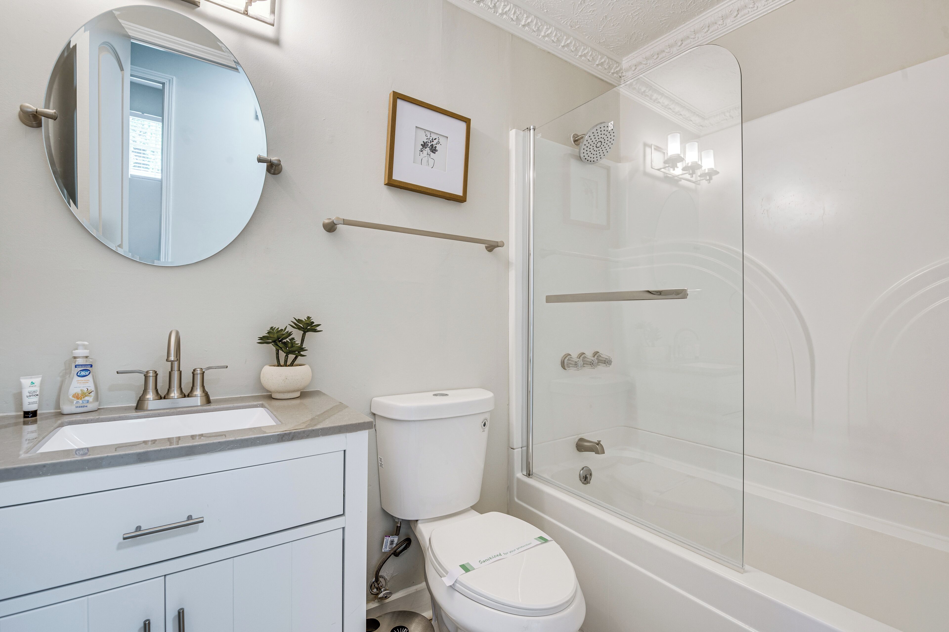 A bathroom with a round mirror, a toilet, a sink, and a shower.