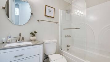 A bathroom with a round mirror, a toilet, a sink, and a shower.