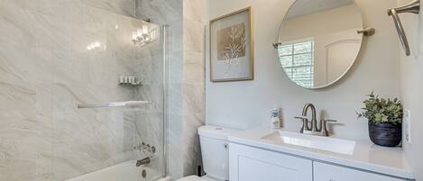 A modern bathroom with a glass shower enclosure, a white toilet, a sink with a mirror, and a potted plant.
