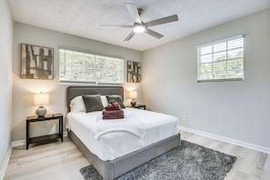 A bedroom with a bed, two bedside tables, a ceiling fan, and two windows with blinds.