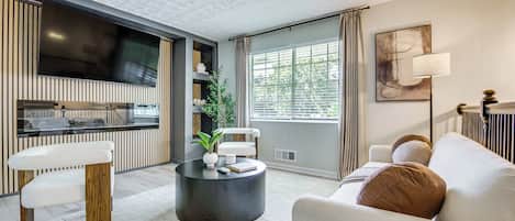 A modern living room with a flat-screen TV, a round coffee table, a sofa, and a large window with curtains.