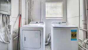 A laundry room with two washing machines, a window with blinds, and visible plumbing.