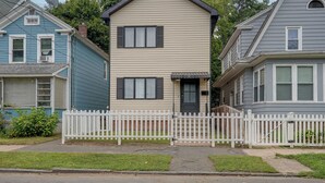 Uma casa de dois andares com cerca branca de piquete, uma porta da frente e um pequeno alpendre.