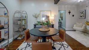 Uma sala de estar moderna com uma mesa de jantar redonda, cadeiras de couro, uma estante de livros, um vaso com flores e um quadro na parede.