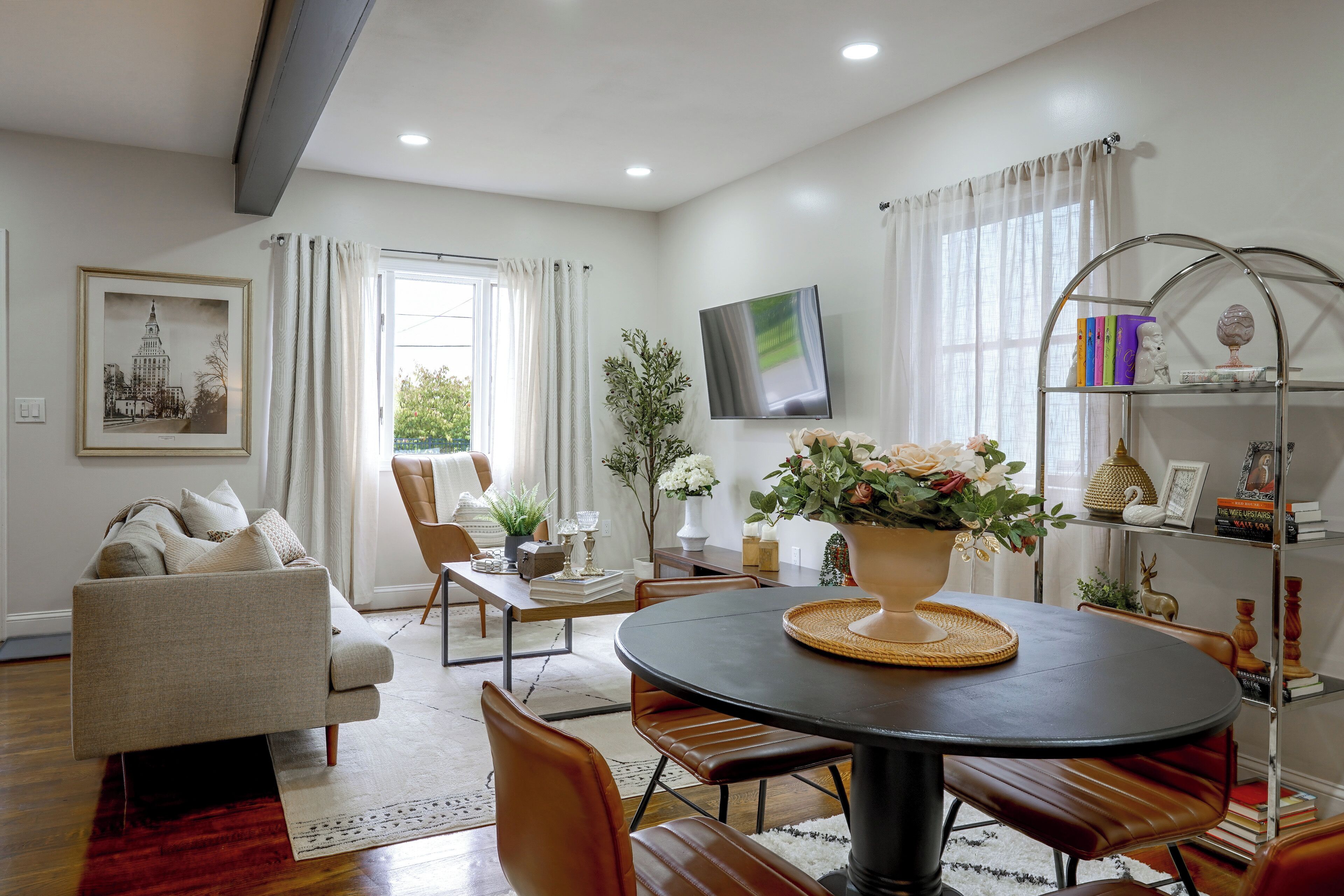 A modern living room with a sofa, dining table, chairs, a TV, and a bookshelf.