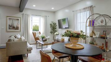A modern living room with a sofa, dining table, chairs, a TV, and a bookshelf.