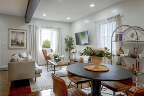 A modern living room with a sofa, dining table, chairs, a TV, and a bookshelf.