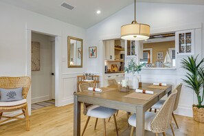 A dining area with a wooden table, wicker chairs, and a hanging light fixture. - Stroll to Redondo Beach: Modern, Coastal Gem (Redondo Beach)