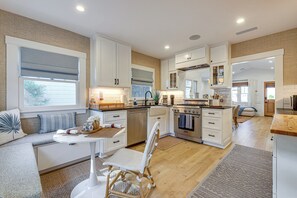 A modern kitchen with white cabinetry, a dining area with a round table, and a view of the outside through large windows.