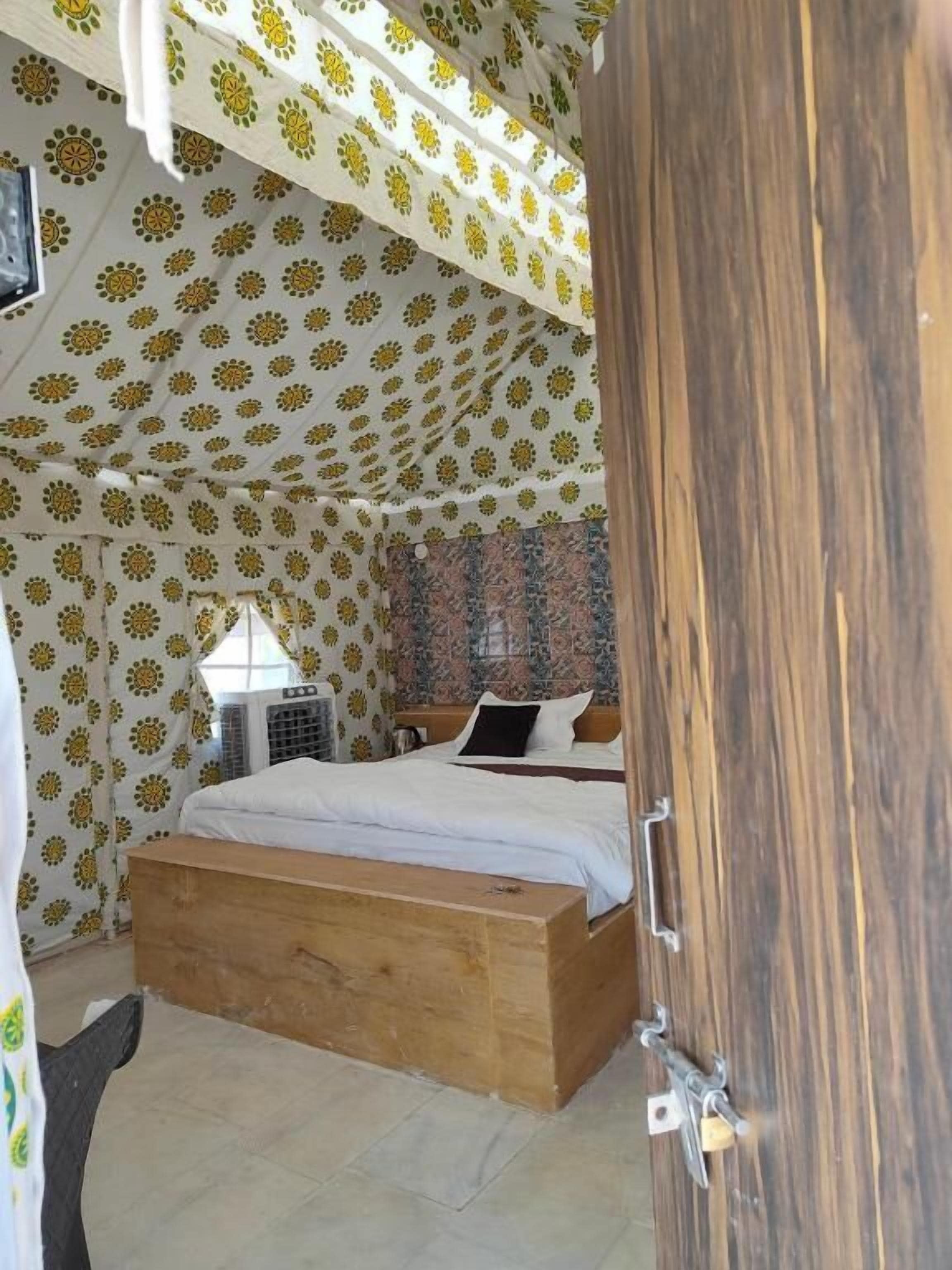A room with a bed, a wooden bench, patterned curtains, and a window with an air conditioning unit.