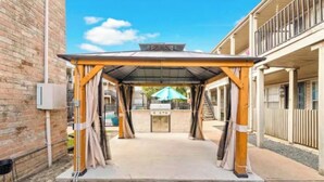 A covered outdoor area with a grill, surrounded by brick walls and a building with balconies. - Cozy 2-bedroom townhome by Galleria Houston with Pool & BBQ (Houston)