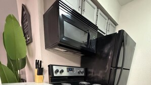 A kitchen with a stainless steel refrigerator, a black microwave, a stove with four burners, and a marble countertop. - Cozy 2-bedroom townhome by Galleria Houston with Pool & BBQ (Houston)